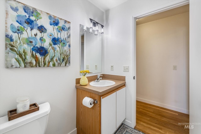 bathroom with baseboards, toilet, wood finished floors, and vanity