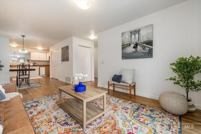 living area with wood finished floors, visible vents, a chandelier, and baseboards