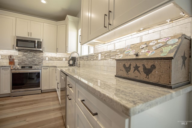 kitchen featuring light hardwood / wood-style flooring, white cabinetry, stainless steel appliances, light stone countertops, and decorative backsplash