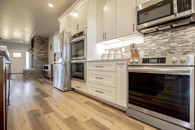 kitchen with white cabinetry, light stone counters, tasteful backsplash, stainless steel appliances, and light hardwood / wood-style floors