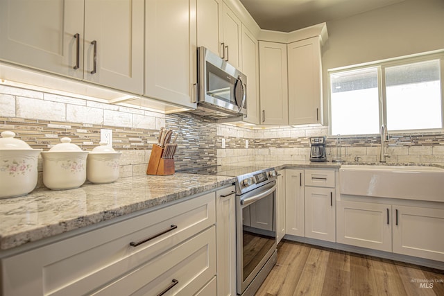 kitchen featuring sink, white cabinetry, light hardwood / wood-style flooring, stainless steel appliances, and light stone countertops