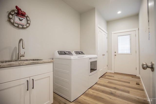 clothes washing area with sink, light hardwood / wood-style flooring, and washing machine and clothes dryer