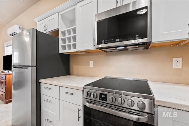 kitchen with appliances with stainless steel finishes, a wall unit AC, white cabinets, and light stone counters