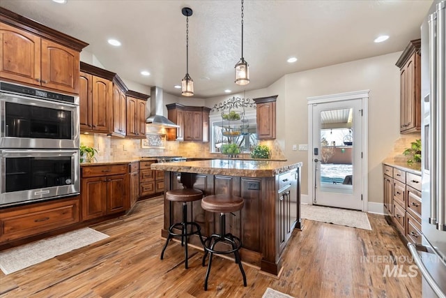 kitchen featuring wood-type flooring, decorative backsplash, a center island, stainless steel appliances, and wall chimney exhaust hood