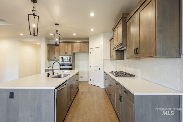 kitchen with a large island with sink, appliances with stainless steel finishes, sink, and hanging light fixtures