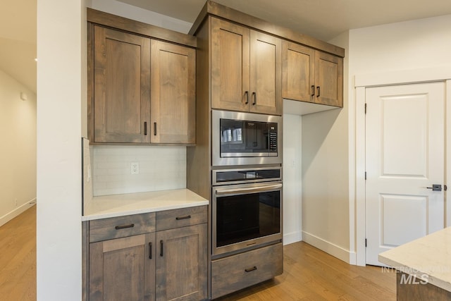 kitchen featuring tasteful backsplash, built in microwave, oven, and light hardwood / wood-style flooring