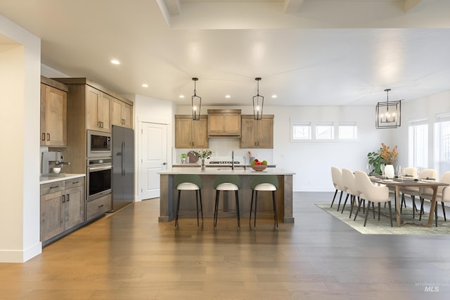 kitchen featuring dark hardwood / wood-style flooring, hanging light fixtures, a center island with sink, and appliances with stainless steel finishes