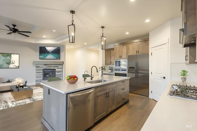 kitchen with a fireplace, sink, hanging light fixtures, built in appliances, and a center island with sink