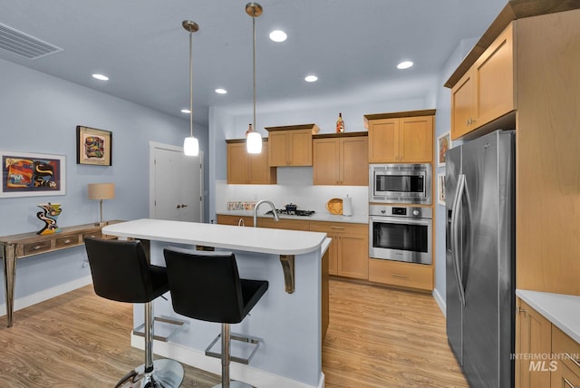 kitchen featuring pendant lighting, an island with sink, stainless steel appliances, light wood-type flooring, and a kitchen breakfast bar