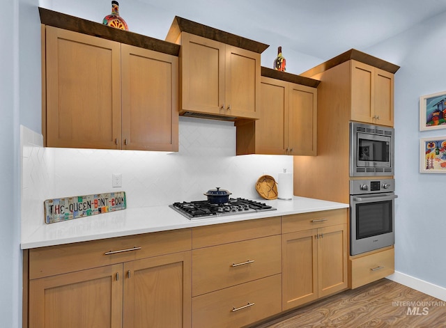 kitchen featuring light brown cabinets, light wood-type flooring, backsplash, and appliances with stainless steel finishes