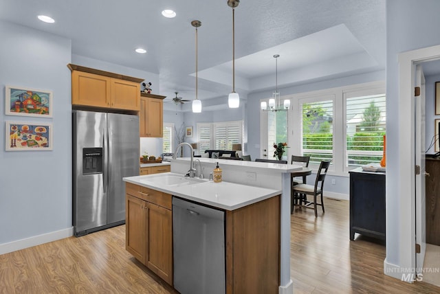 kitchen with stainless steel appliances, a raised ceiling, an island with sink, ceiling fan with notable chandelier, and sink