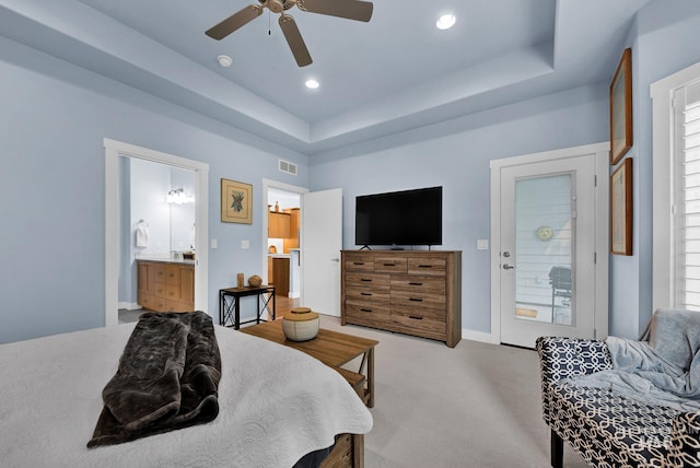 bedroom featuring ensuite bath, a raised ceiling, light colored carpet, and ceiling fan