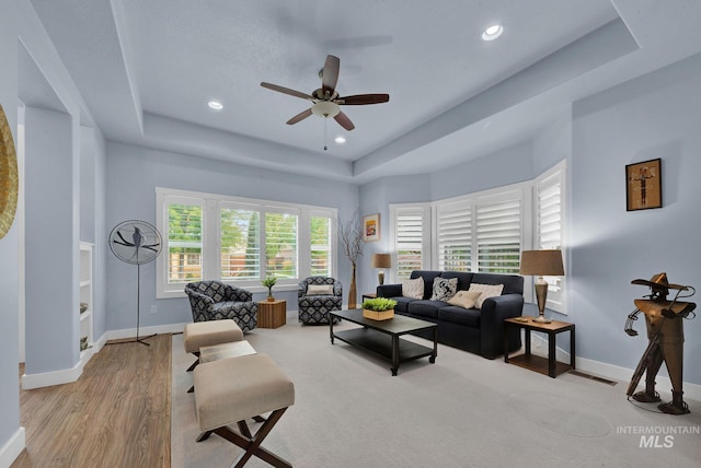 living room with ceiling fan, light wood-type flooring, and a raised ceiling