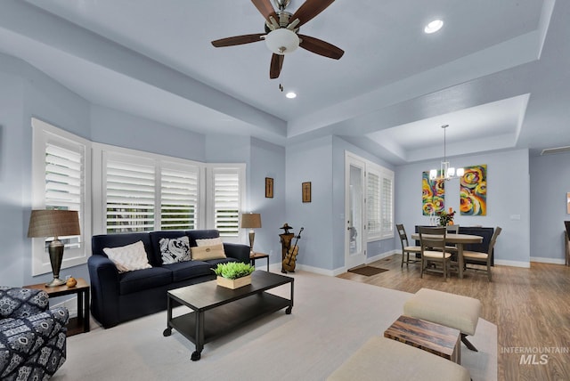 living room with ceiling fan with notable chandelier, hardwood / wood-style floors, and a tray ceiling