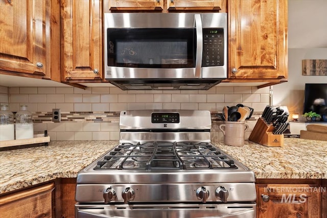 kitchen with light stone counters, stainless steel appliances, tasteful backsplash, and brown cabinetry