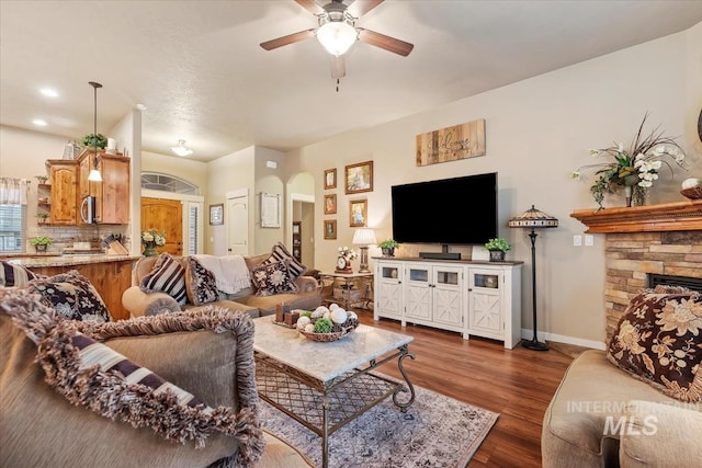 living room with baseboards, ceiling fan, dark wood finished floors, a fireplace, and arched walkways