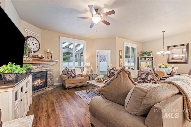 living room with a fireplace, ceiling fan with notable chandelier, and dark wood-style floors