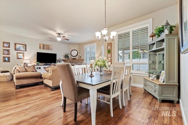 dining space featuring baseboards, light wood-style floors, and ceiling fan with notable chandelier