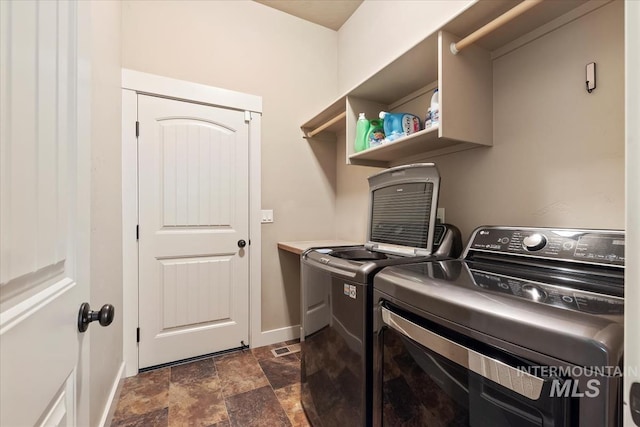 laundry room with laundry area, stone finish flooring, baseboards, and separate washer and dryer