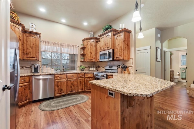 kitchen with a peninsula, arched walkways, a sink, stainless steel appliances, and light wood-style floors