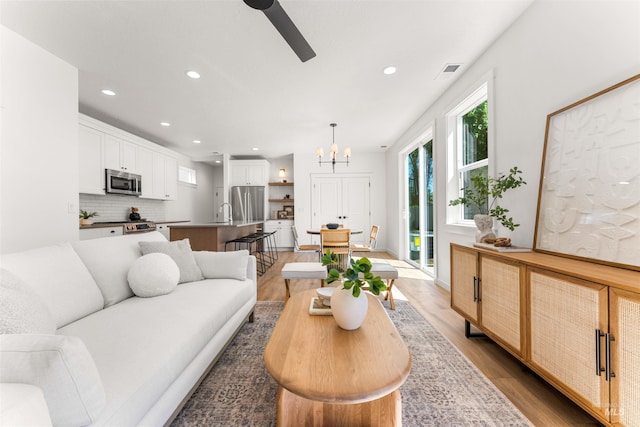 living room with light hardwood / wood-style floors and ceiling fan with notable chandelier