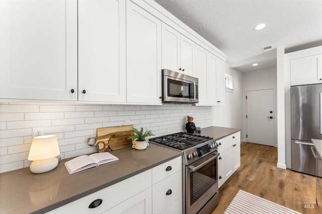 kitchen with backsplash, appliances with stainless steel finishes, a textured ceiling, white cabinetry, and dark hardwood / wood-style floors