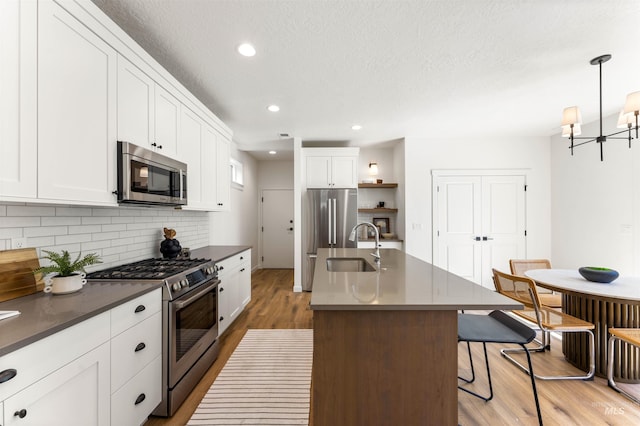 kitchen featuring a center island with sink, hanging light fixtures, appliances with stainless steel finishes, white cabinetry, and wood-type flooring