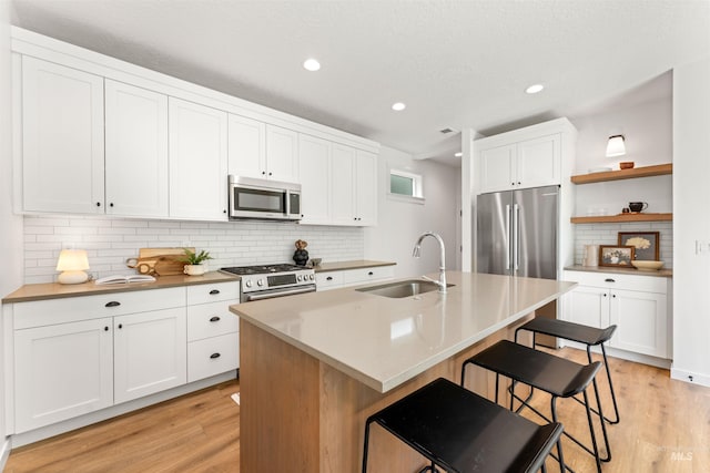 kitchen featuring sink, an island with sink, stainless steel appliances, white cabinets, and a breakfast bar