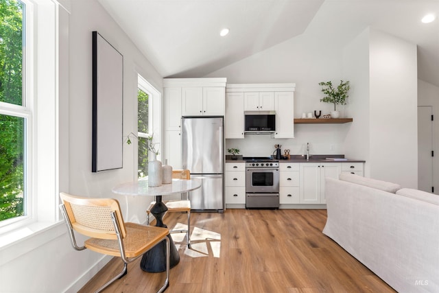 kitchen with appliances with stainless steel finishes, sink, white cabinetry, light hardwood / wood-style floors, and lofted ceiling