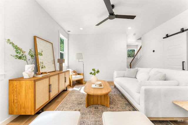 living room with ceiling fan, wood-type flooring, and a barn door