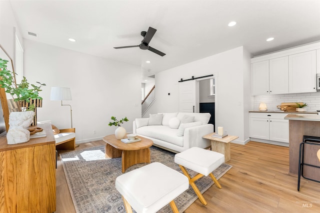 living room with light hardwood / wood-style floors, a barn door, and ceiling fan