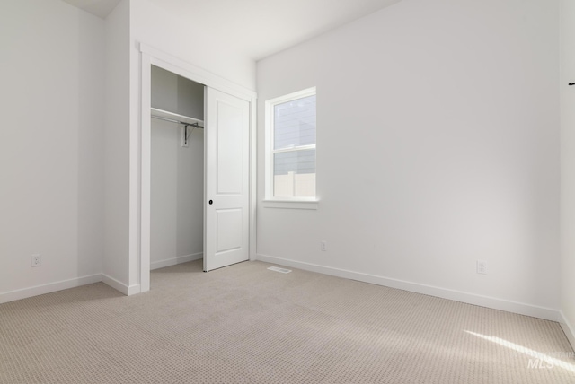 unfurnished bedroom with light colored carpet and a closet