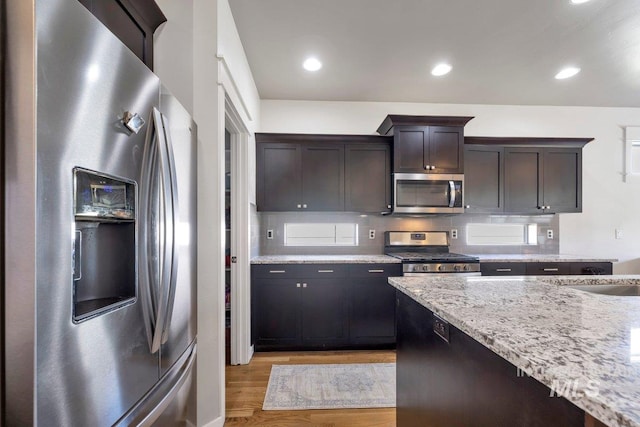 633 Reese Rd, Twin Falls, ID 83301 - kitchen with stainless steel appliances, light wood finished floors, dark brown cabinets, light stone counters, and decorative backsplash