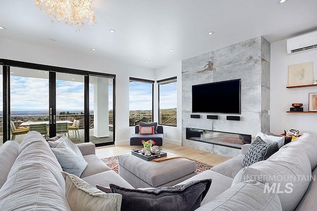 living room with a wall mounted air conditioner, light wood-type flooring, a fireplace, and a chandelier