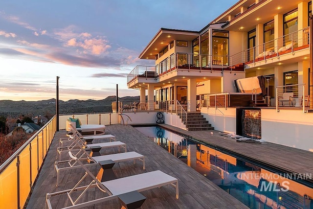 deck at dusk with a mountain view, a fenced in pool, and a patio