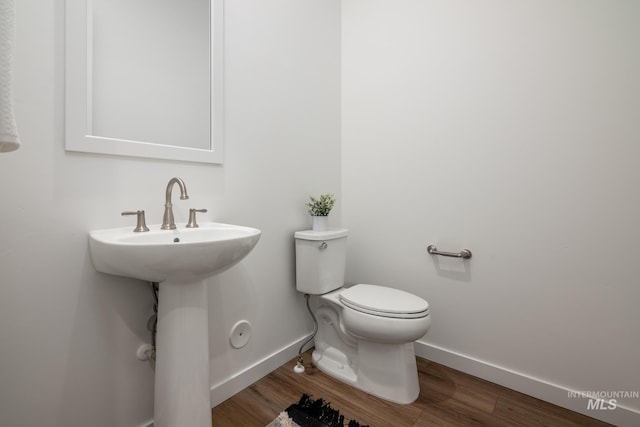 half bathroom featuring baseboards, toilet, wood finished floors, and a sink