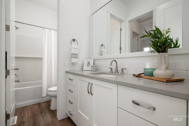 bathroom featuring wood finished floors, toilet, vanity, tasteful backsplash, and shower / tub combo