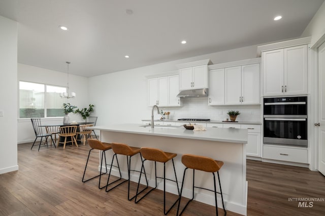 kitchen featuring a sink, double oven, tasteful backsplash, gas cooktop, and under cabinet range hood