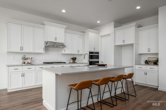 kitchen featuring a sink, a center island with sink, gas cooktop, under cabinet range hood, and white cabinets
