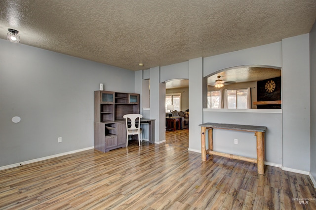 living area featuring baseboards, ceiling fan, wood finished floors, arched walkways, and a textured ceiling