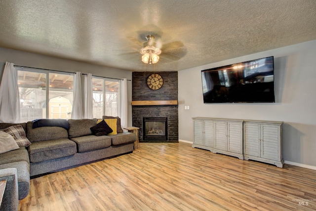 living area with a ceiling fan, wood finished floors, baseboards, a fireplace, and a textured ceiling