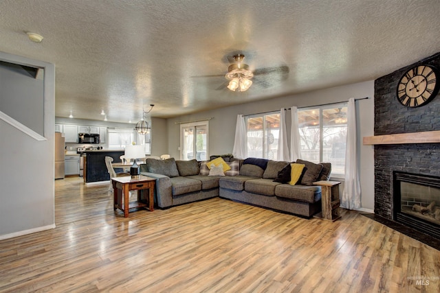 living room featuring a textured ceiling, a stone fireplace, light wood-style flooring, and a ceiling fan