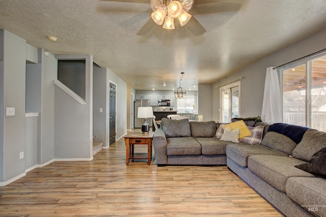 living area featuring light wood-type flooring, baseboards, a textured ceiling, and ceiling fan