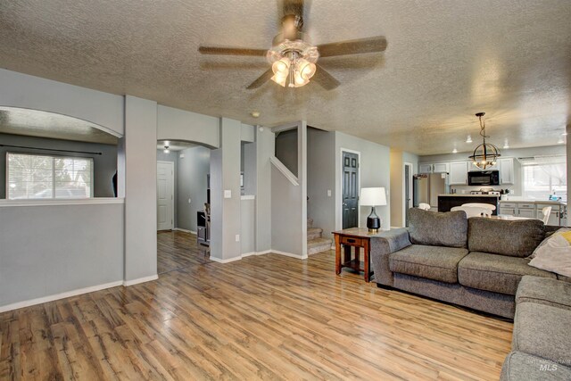 living area with stairs, light wood-type flooring, arched walkways, a textured ceiling, and a ceiling fan