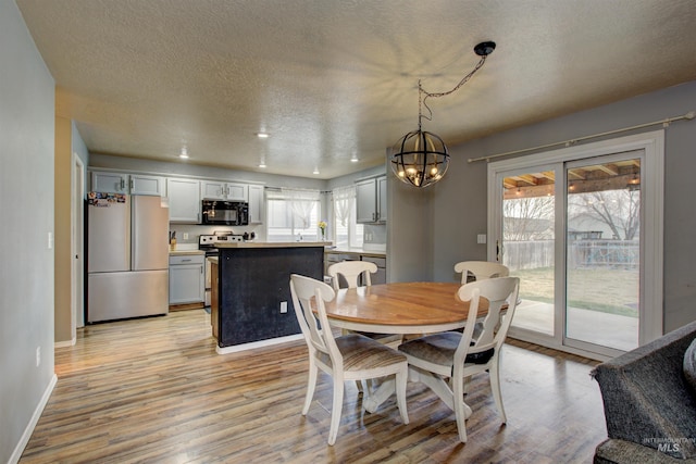 dining room featuring a textured ceiling, light wood-style floors, baseboards, and a chandelier