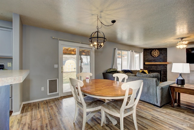 dining area featuring a large fireplace, baseboards, a chandelier, light wood-style flooring, and a textured ceiling