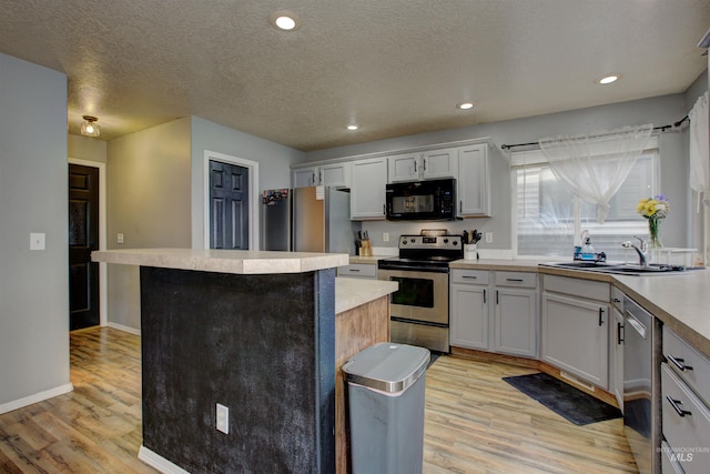 kitchen with a sink, a kitchen island, light wood finished floors, and stainless steel appliances