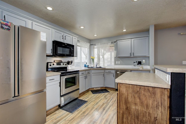 kitchen featuring light countertops, light wood-type flooring, appliances with stainless steel finishes, and a sink