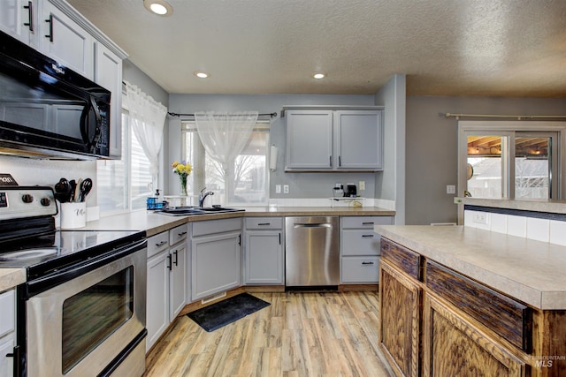 kitchen with light wood-style flooring, a sink, a textured ceiling, appliances with stainless steel finishes, and light countertops