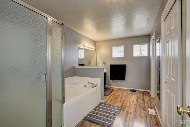 full bathroom with a bath, a shower stall, a textured ceiling, and wood finished floors